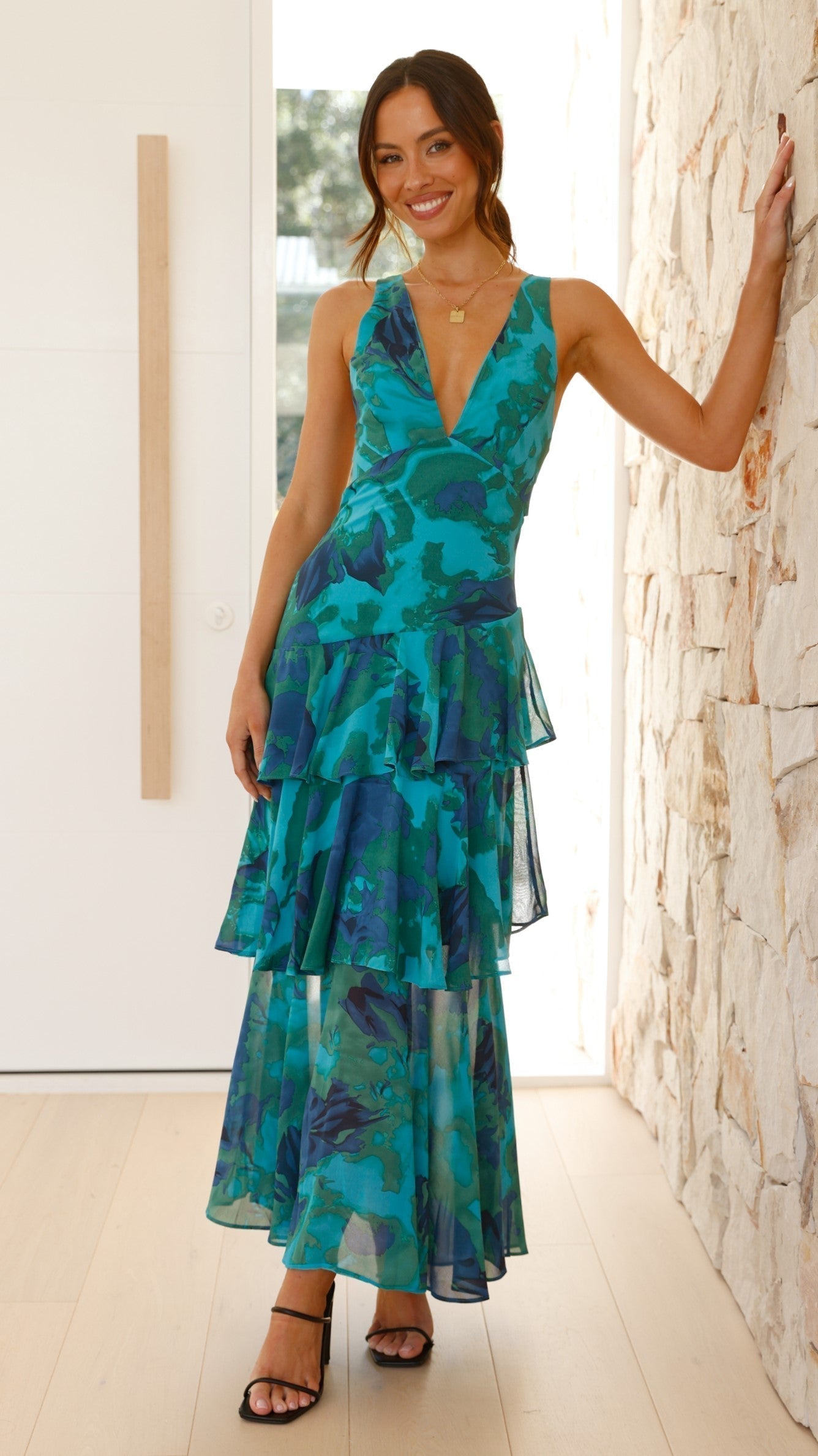 Yellow - A woman wearing a vibrant teal and blue abstract floral print maxi dress featuring a deep V-neckline and a dramatic tiered ruffle skirt.