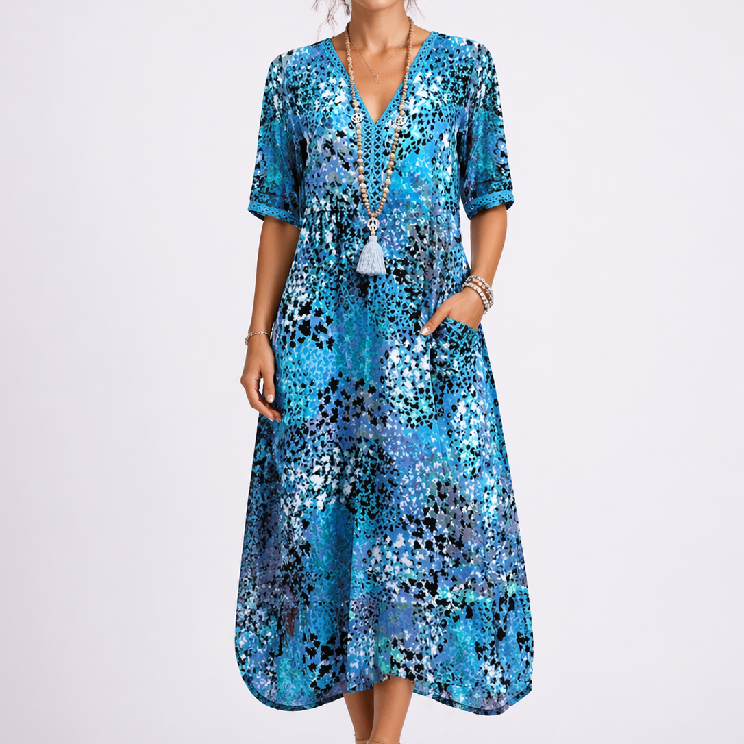 Blue - Woman wearing a relaxed fit abstract print midi dress with short sleeves, a V-neckline, and side pockets against a plain background.