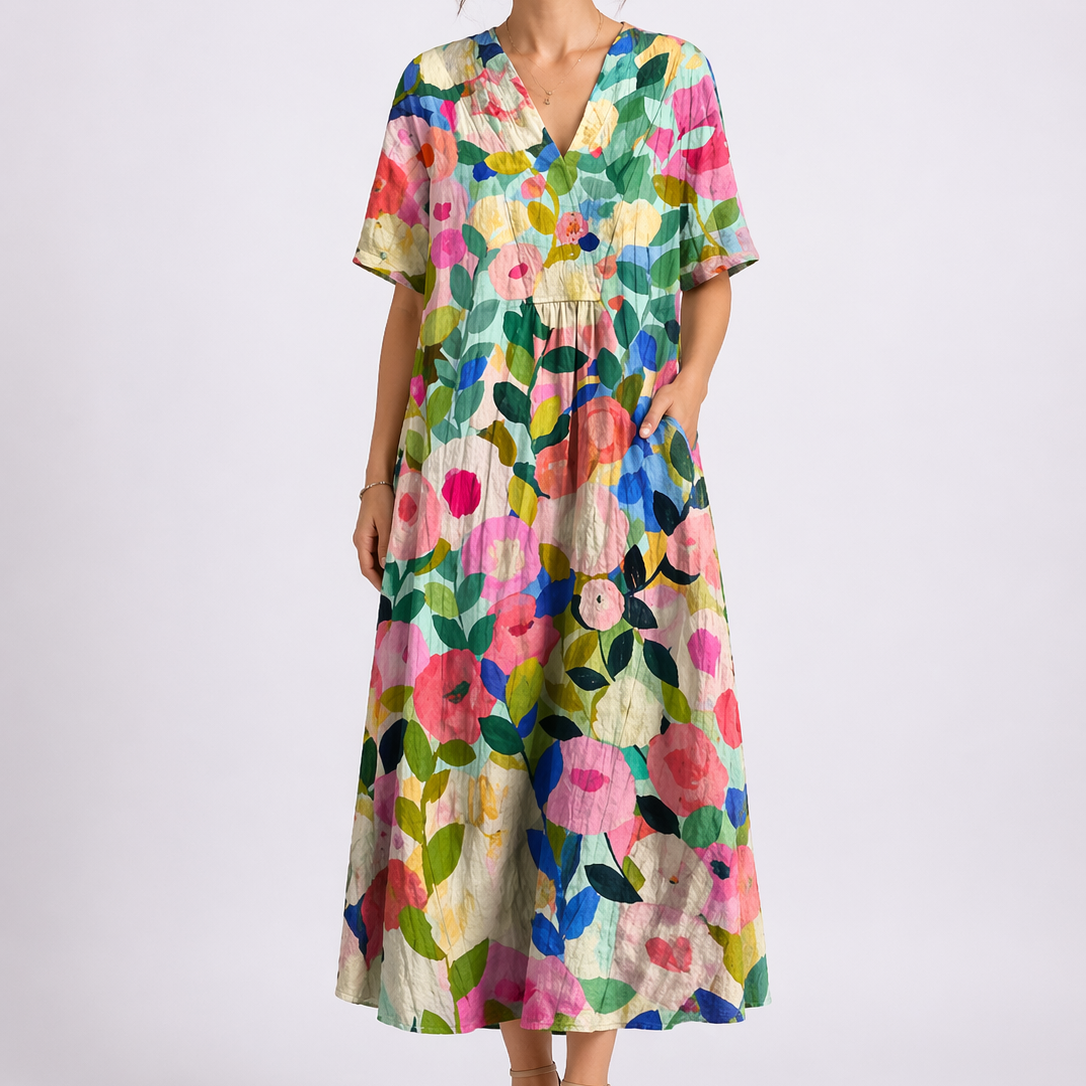 Floral - Model wearing a woven floral V-neck midaxi dress with short sleeves and side pockets against a plain grey background.