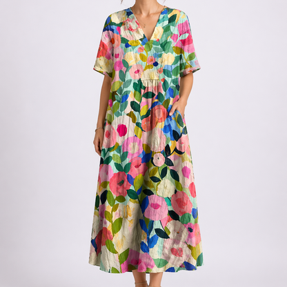 Floral - Model wearing a woven floral V-neck midaxi dress with short sleeves and side pockets against a plain grey background.