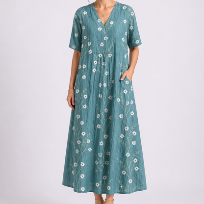 Turquoise - Model wearing a woven floral V-neck midaxi dress with short sleeves and side pockets against a plain grey background.