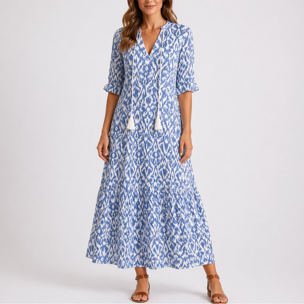Blue - Woman wearing a woven ikat pattern maxi dress with a V-neck, tassel ties, 3/4-sleeves, and a tiered hemline against a light grey background.