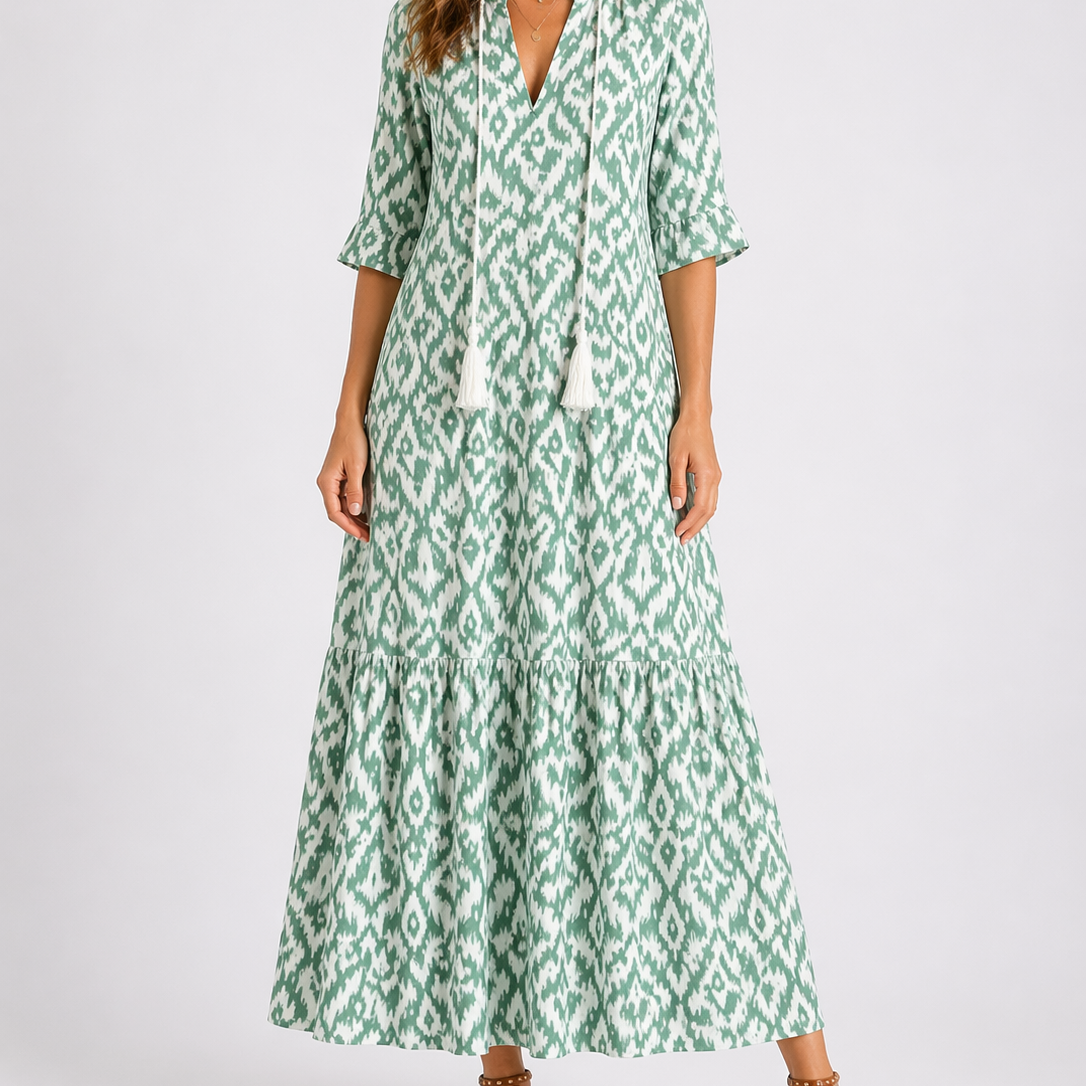 Light green - Woman wearing a woven ikat pattern maxi dress with a V-neck, tassel ties, 3/4-sleeves, and a tiered hemline against a light grey background.