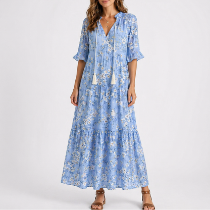 Blue & White - Woman wearing a woven ikat pattern maxi dress with a V-neck, tassel ties, 3/4-sleeves, and a tiered hemline against a light grey background.