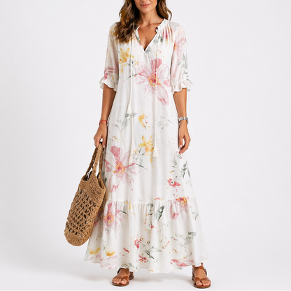 White - Woman wearing a woven ikat pattern maxi dress with a V-neck, tassel ties, 3/4-sleeves, and a tiered hemline against a light grey background.