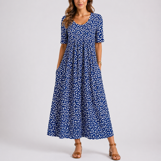 Blue - Model wearing a printed short-sleeve midaxi dress with a scoop neckline, gathered waist, and side pockets, standing against a plain light grey background.