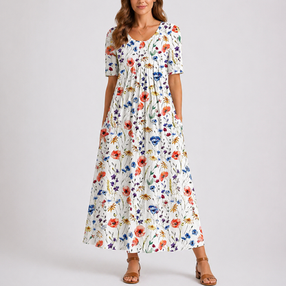 Floral - Model wearing a printed short-sleeve midaxi dress with a scoop neckline, gathered waist, and side pockets, standing against a plain light grey background.