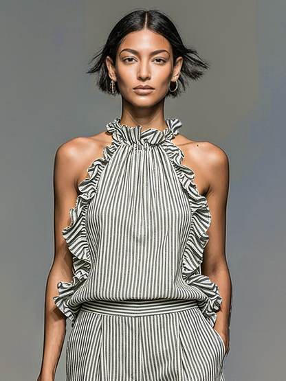 Photo Color - A model walking on a runway wearing a striped two-piece set featuring a ruffled halter top and pleated shorts, carrying a woven straw tote bag.
